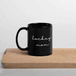 May include: Black ceramic coffee mug with white text that reads "hockey mom".