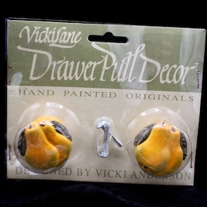 May include: Two hand-painted pear drawer pulls with a green stem and leaves. The pulls are packaged on a card that reads "Vicki Jane Drawer Pull Decor Hand Painted Originals Designed by Vicki Anderson".