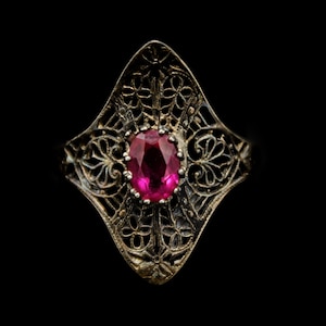 May include: A silver ring with a filigree design and a large, oval-shaped, pink gemstone.