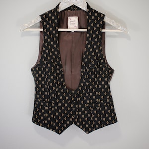May include: A black and gold patterned vest with a V-neck and a brown lining. The vest has a label that says "Giselle Lepore".