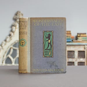 May include: Two vintage books titled "Wonder Tales of the East" by Donald A. Mackenzie. The book on the left has a tan spine with green and gold accents. The book on the right has a blue cover with a green and black illustration.