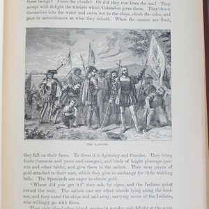 May include: A vintage black and white illustration shows explorers landing on a shore, interacting with indigenous people. The scene features figures in historical attire, holding flags. The image is from a book.