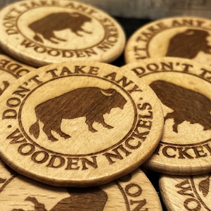 May include: A collection of wooden nickels with a bison silhouette and the text "DON'T TAKE ANY WOODEN NICKELS" engraved around the edge. The nickels are light brown with a darker brown bison design.