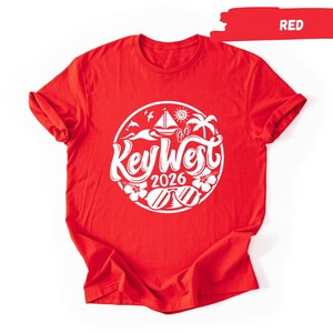 A red t-shirt with a white graphic design featuring a circular logo with the text "Key West" and "2026" printed on it.