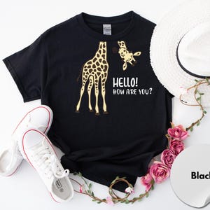 A black t-shirt with a giraffe and the text "Hello! How are you?" printed on it, along with a white hat and some pink flowers.