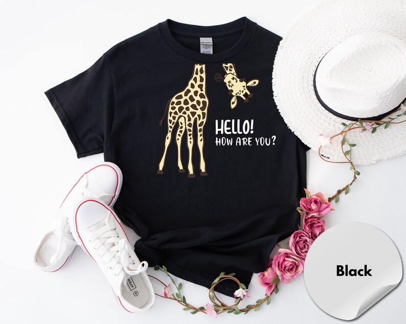 A black t-shirt with a giraffe and the text "Hello! How are you?" printed on it, along with a white hat and some pink flowers.