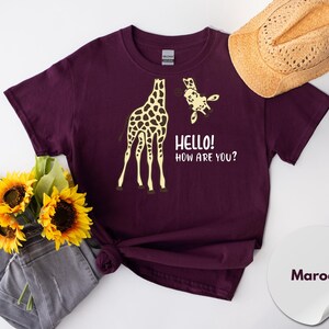 a maroon t-shirt with a graphic of a giraffe and the text "Hello! How Are You?" printed on it, along with a straw hat and a bouquet of sunflowers.
