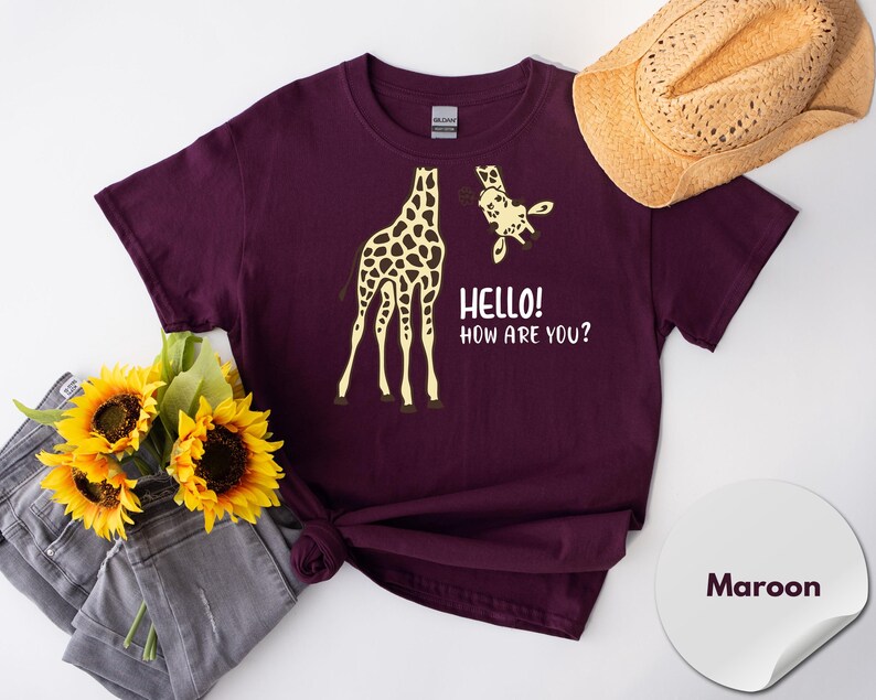 a maroon t-shirt with a graphic of a giraffe and the text "Hello! How Are You?" printed on it, along with a straw hat and a bouquet of sunflowers.
