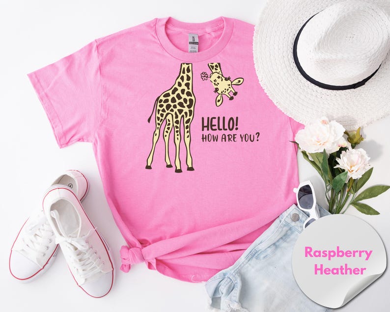 A pink t-shirt with a giraffe and the text "Hello! How Are You?" printed on it, along with a white hat, sunglasses, and a pair of white sneakers. There are also some flowers and a white circular sticker with the text "Raspberry Heather" on the right side of the image.