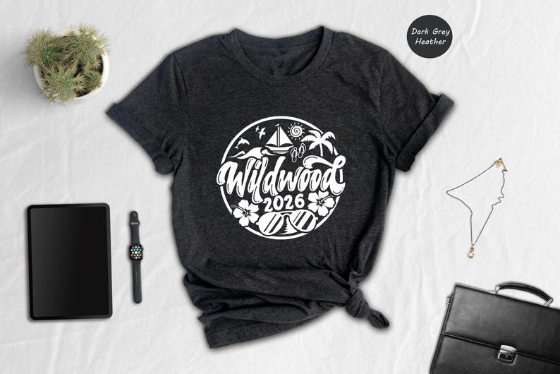 a casual outfit laid out on a white surface, including a black t-shirt with a graphic design, a tablet, a watch, a potted plant, and a black bag.
