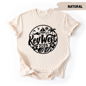 A beige t-shirt with a black graphic design featuring the text "Key West 2016" and various icons related to the location.