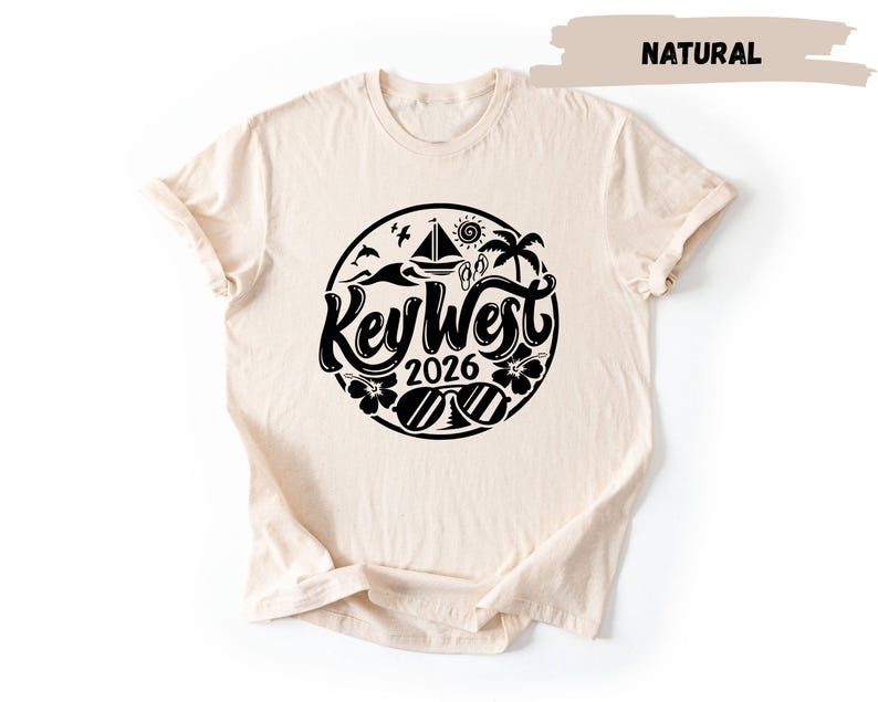 A beige t-shirt with a black graphic design featuring the text "Key West 2016" and various icons related to the location.