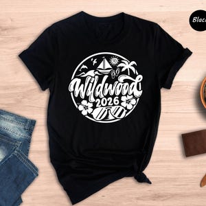 a black t-shirt with a white graphic design, a pair of blue jeans, a brown wallet, a watch, and a potted plant on a wooden surface.