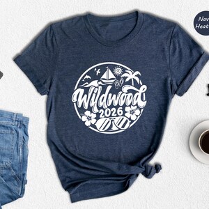 a casual outfit consisting of a navy blue t-shirt with a white graphic design, a pair of blue jeans, a black wallet, a pair of glasses, a white coffee cup, and a black pen.