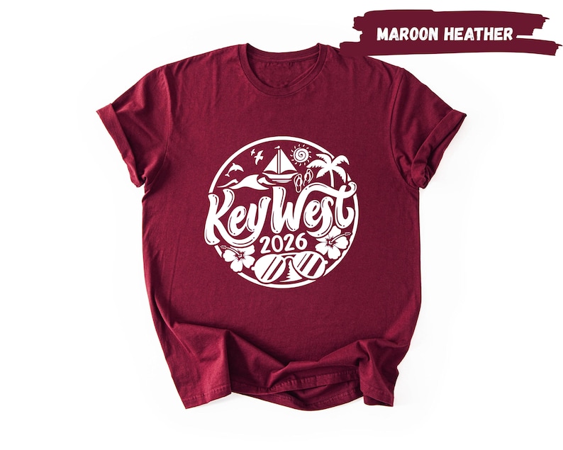 A maroon t-shirt with a white graphic design featuring the text "Key West" and "2016" surrounded by various beach and ocean-themed illustrations.