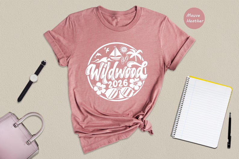 a pink t-shirt with a white graphic design, a watch, a notebook, a pen, and a pink handbag arranged on a beige background.