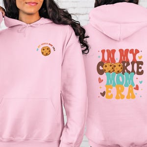 a woman wearing a pink hoodie with a cookie on it
