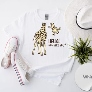 a white t-shirt with a giraffe graphic and the text "Hello! How Are You?" printed on it, along with a pair of white sneakers and a white hat.