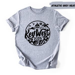A grey t-shirt with a graphic design featuring the text "Key West" and the year "2026" surrounded by various symbols and icons related to the location.