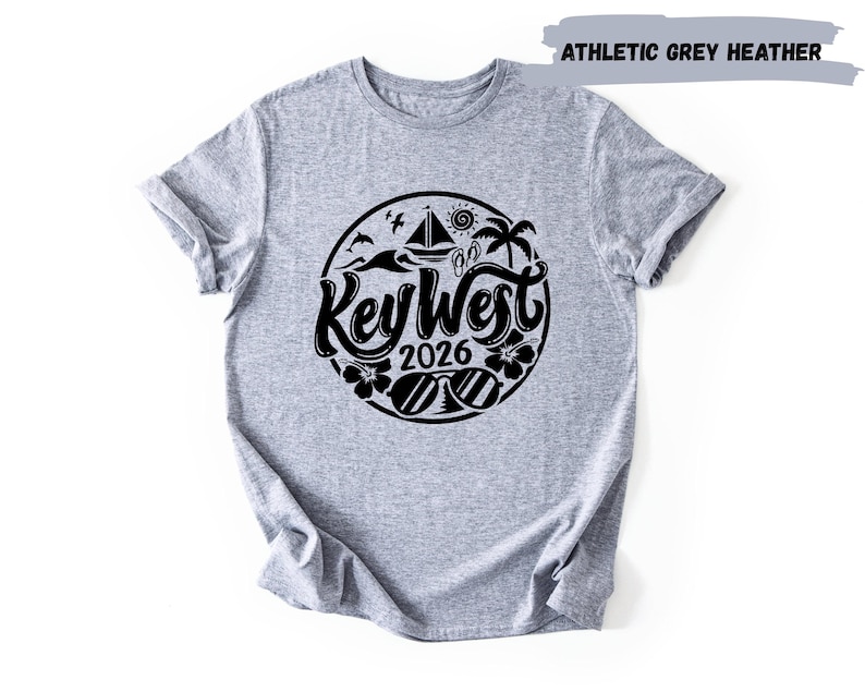 A grey t-shirt with a graphic design featuring the text "Key West" and the year "2026" surrounded by various symbols and icons related to the location.