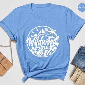 A blue t-shirt with a white graphic design, a brown purse, and a pair of denim shorts are arranged on a white background.