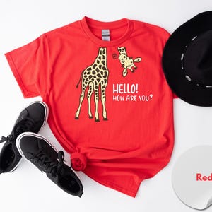 a red t-shirt with a giraffe graphic and the text "Hello! How are you?" along with a pair of black sneakers and a black hat.