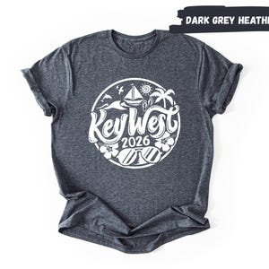 A gray t-shirt with a graphic design featuring a circular logo with the text "Key West" and the year "2026" printed on it.