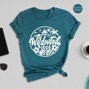 a teal t-shirt with a white graphic design, a pair of sunglasses, a tablet, a cup of coffee, and a hat, all arranged on a light gray background.
