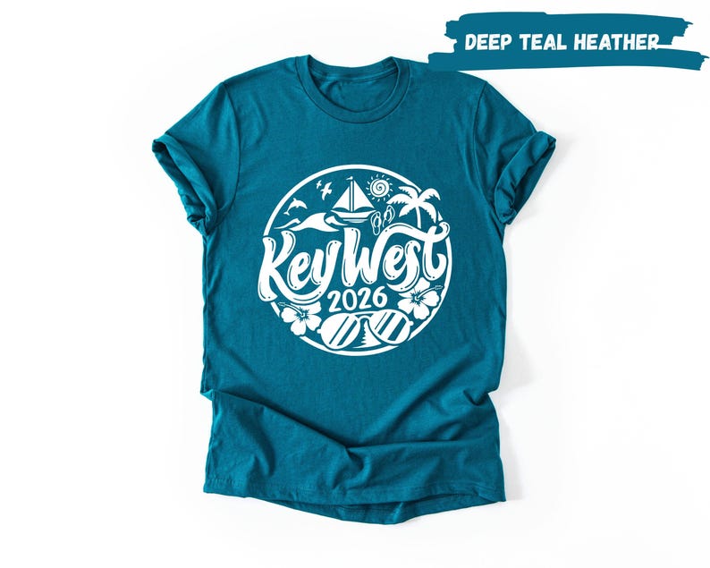 A teal-colored t-shirt with a white graphic design featuring a circular motif with various beach and ocean-themed elements, such as palm trees, surfboards, and a sailboat.