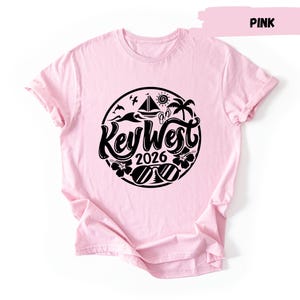 A pink t-shirt with a graphic design featuring a circular logo with the text "Key West 2016" and various icons related to the beach and ocean.