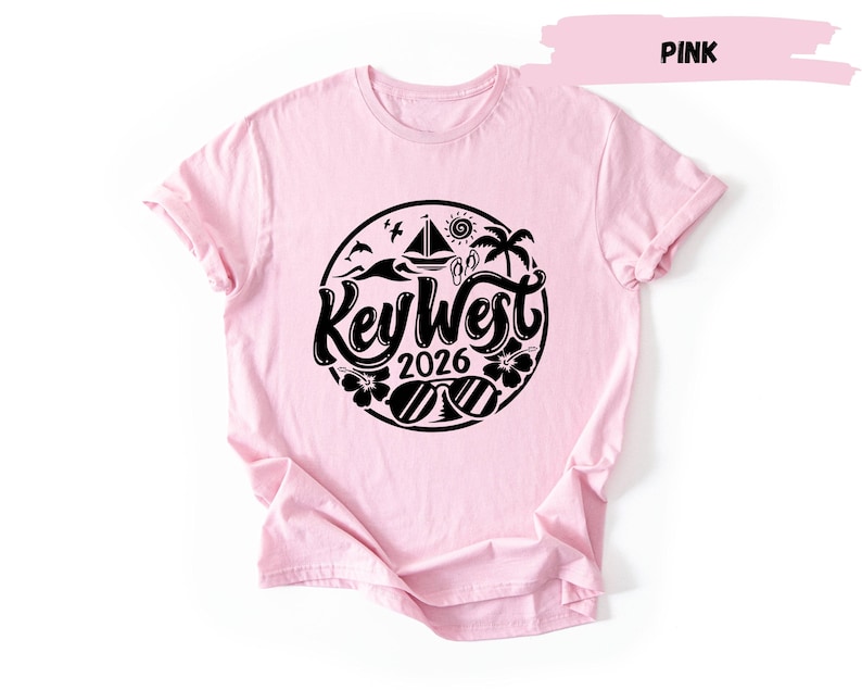 A pink t-shirt with a graphic design featuring a circular logo with the text "Key West 2016" and various icons related to the beach and ocean.