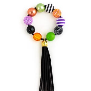 May include: A vibrant beaded necklace with a black tassel. The necklace showcases a range of round beads in colours such as orange, green, purple, and black. Some beads have patterns, and the tassel is made of black strands.