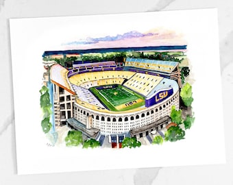 May include: A watercolor painting of Tiger Stadium, home of the LSU Tigers football team. The stadium is shown from an aerial view, with the field and stands visible. The stadium is surrounded by trees and a blue sky with pink clouds.