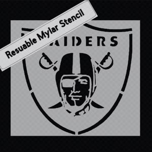 May include: A black and white stencil featuring the Raiders logo, including a helmeted face, crossed swords, and the word "RAIDERS." The stencil is on a transparent background with the text "Resuable Mylar Stencil" in a white rectangle.