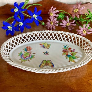 May include: White oval serving dish with a woven rim and a floral design featuring butterflies. The dish is on a wooden surface.