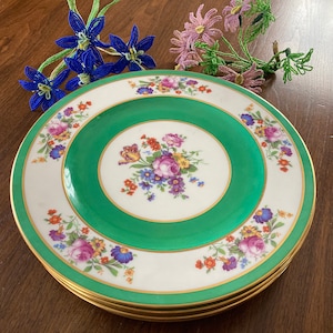 May include: A set of three white ceramic dinner plates with a green center and gold trim. The plates are decorated with a floral pattern in shades of pink, purple, yellow, and orange.