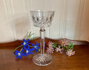 May include: A clear, cut-crystal stemmed glass with a wide bowl and a starburst base. Beaded blue and pink flowers are arranged around the glass on a wooden surface. The glass is likely for serving a beverage.