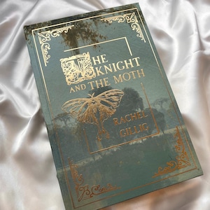 Puede incluir: Un libro de tapa dura titulado "The Knight and the Moth" de Rachel Gillig. La portada es de color turquesa con letras doradas y una ilustración de una polilla. Bordes dorados adornan el título y el nombre del autor.