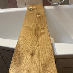 Könnte beinhalten: Ein Holz-Badetablett mit natürlicher Holzoptik. Das Tablett liegt am Rand einer weißen Badewanne. Auf dem Tablett befindet sich eine kleine weiße Kerze.