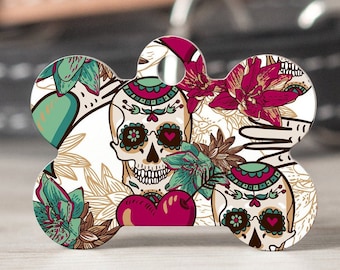 May include: A white bone-shaped dog tag with a colorful floral design featuring two sugar skulls with hearts and flowers.