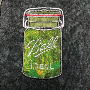 Könnte beinhalten: Ein grünes Glasgefäß mit einem weißen Etikett, auf dem "Ball" und "IDEAL" steht. Das Gefäß hat einen weißen Deckel mit einem roten Gummiring.
