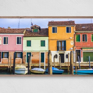 Könnte beinhalten: Eine Reihe von bunten Häusern mit roten Ziegeldächern säumen einen Kanal in Venedig, Italien. Die Häuser sind in Pink, Grün, Orange und Rot gestrichen. Vor den Häusern liegen Boote an.