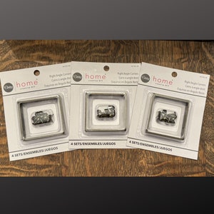 May include: Three packages of Dritz Home Creative DIY right angle corners. Each package contains four sets of silver corner brackets and a small bag of black screws. The packaging is white with black text and a black and white logo. The text on the packaging reads "Right Angle Corners, Coins à angle droit, Esquinas en Angulo Recto, 4 SETS/ENSEMBLES/JUEGOS".