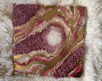 Könnte beinhalten: Quadratisches Kunstwerk aus Kunstharz mit Geoden-Design. Das Kunstwerk zeigt einen zentralen Cluster aus weißen Kristallen, umgeben von Schichten aus goldenem, rosa und rotem Kunstharz. Die Ränder sind mit roten, kristallartigen Elementen strukturiert.