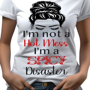 May include: White t-shirt with a black and white illustration of a woman with a messy bun. The text "I'm not a Hot Mess I'm a SPICY Disaster" is printed in black and red on the shirt.