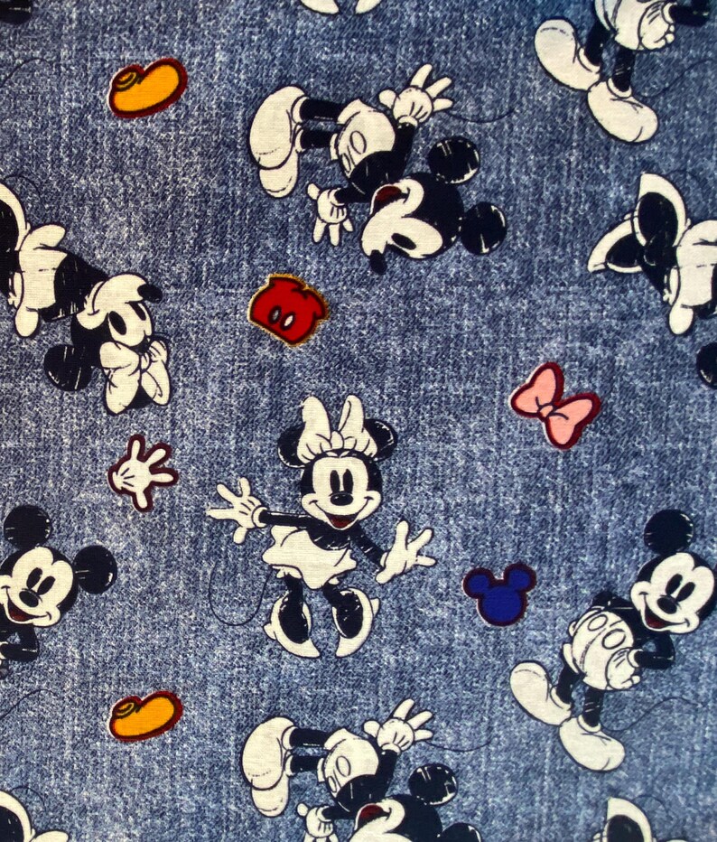 May include: A blue denim fabric featuring a repeating pattern of Mickey Mouse and Minnie Mouse characters in black and white, interspersed with small colorful icons including yellow shoes, red shorts, pink bows, and blue mouse ear silhouettes.