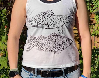 May include: White tank top with a black fish illustration. The sleeveless shirt is paired with blue jeans and a black belt. The design features two detailed fish drawings in black ink.