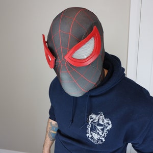 Puede incluir: Una máscara de Spider-Man negra y roja con un patrón de telaraña y cubiertas oculares de malla. La máscara se usa con una sudadera con capucha azul marino. Es un artículo de cosplay.