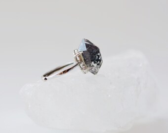 Op de afbeelding: Een zilveren ring met een grote, heldere, gefacetteerde, zwarte diamantvormige steen.