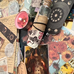 Puede incluir: Una colecci&oacute;n de objetos m&iacute;sticos que incluyen cartas del tarot, peque&ntilde;os frascos de vidrio con tapones de corcho, una vela rosa encendida y papel decorativo. La carta del tarot "The Empress" es visible. Los objetos est&aacute;n dispuestos sobre una superficie con una variedad de colores y texturas.